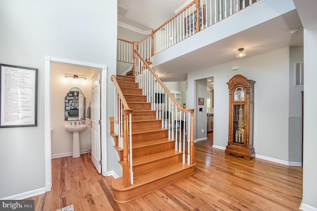 stairs featuring baseboards, ornamental molding, visible vents, wood finished floors, and a high ceiling