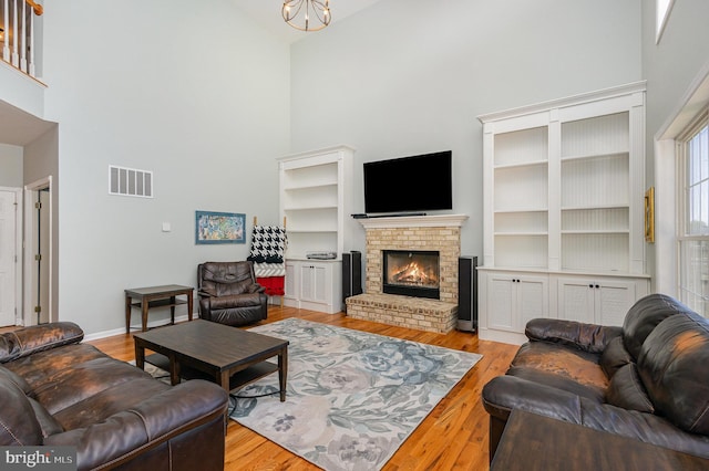 living area with a brick fireplace, high vaulted ceiling, visible vents, and wood finished floors