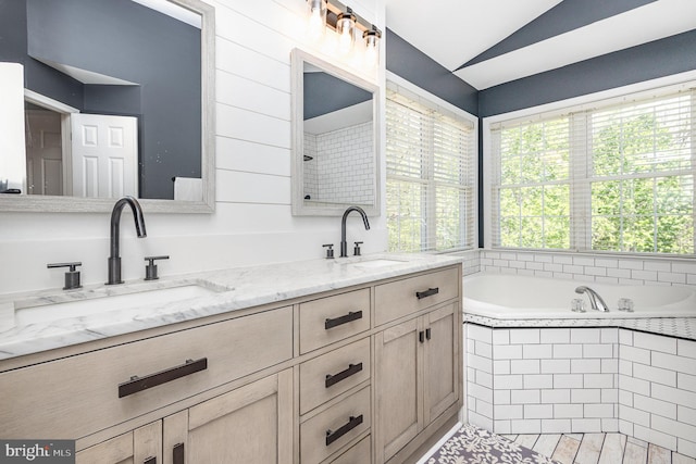 bathroom featuring lofted ceiling, a garden tub, double vanity, and a sink