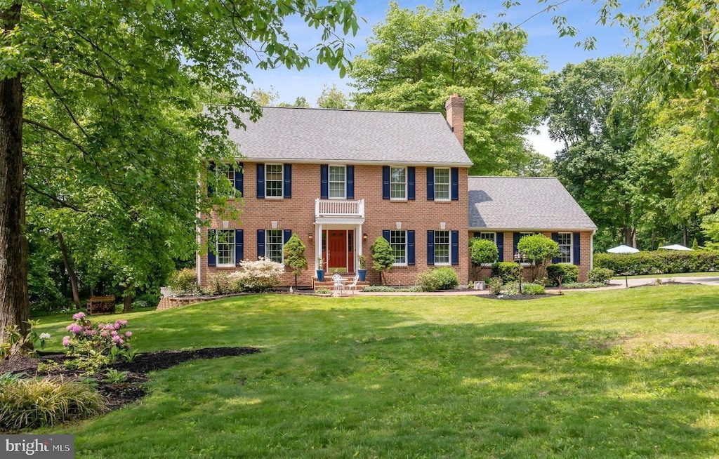 colonial-style house featuring brick siding, a front lawn, and a chimney