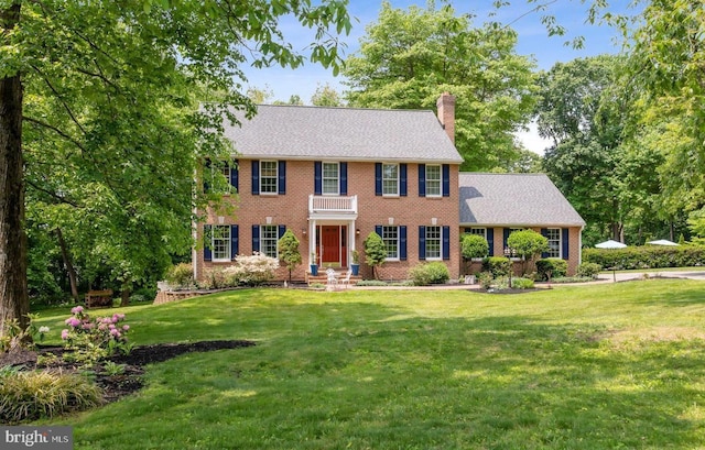 colonial-style house featuring brick siding, a front lawn, and a chimney