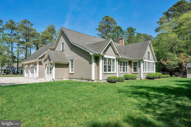 view of front facade with a chimney, an attached garage, a front lawn, a shingled roof, and driveway