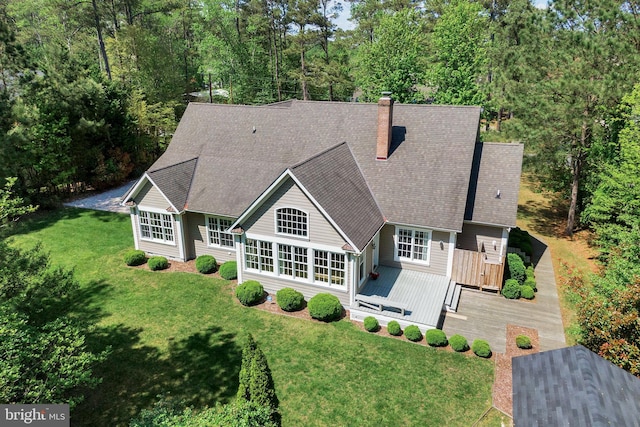 rear view of house featuring a deck, a chimney, a shingled roof, and a lawn