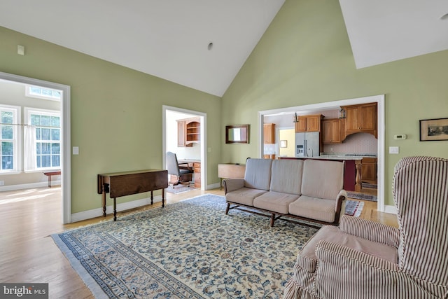 living area featuring light wood-type flooring, baseboards, and high vaulted ceiling