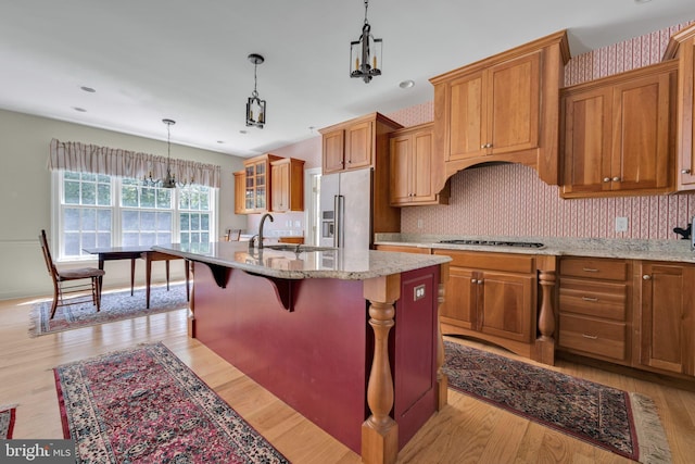 kitchen featuring high quality fridge, brown cabinets, a sink, an island with sink, and light wood-style floors