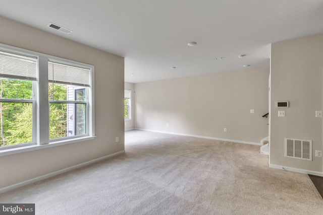 carpeted spare room with visible vents, baseboards, and stairs