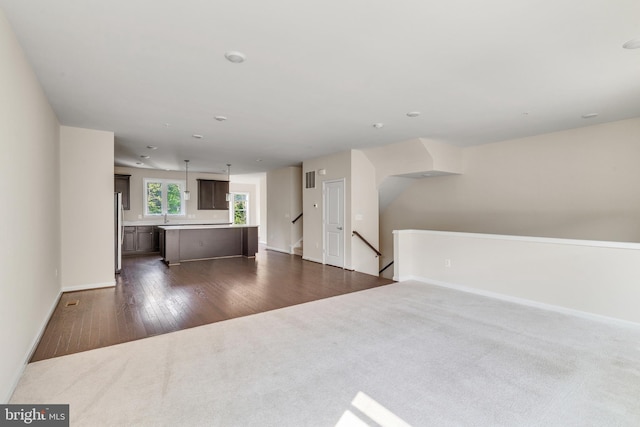 unfurnished living room with baseboards, dark colored carpet, dark wood-style floors, and visible vents