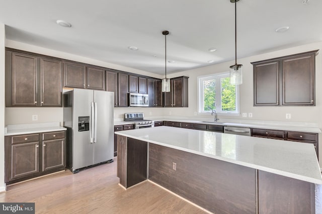 kitchen featuring dark brown cabinetry, a sink, a center island, stainless steel appliances, and light wood-type flooring