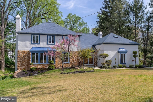 view of front facade featuring a shingled roof, a front lawn, stone siding, and a chimney