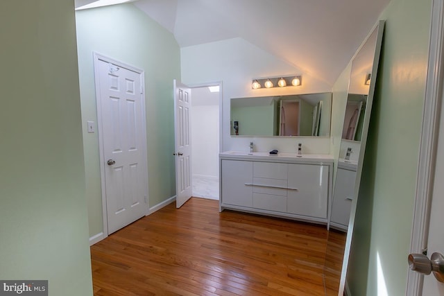 bathroom featuring double vanity, baseboards, hardwood / wood-style floors, and lofted ceiling