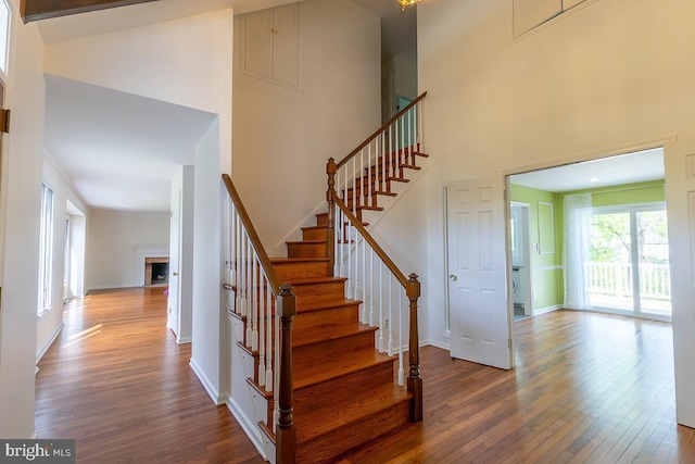stairway featuring a fireplace with flush hearth, baseboards, a high ceiling, and hardwood / wood-style flooring