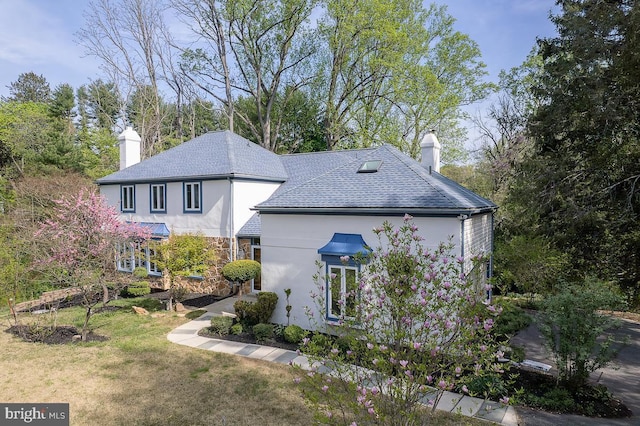 exterior space with a chimney, a yard, stucco siding, and stone siding