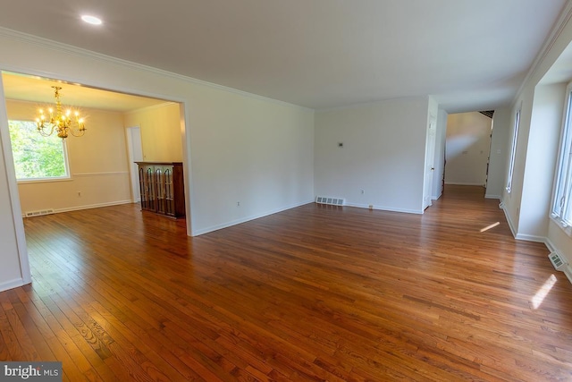 spare room featuring visible vents, hardwood / wood-style flooring, baseboards, an inviting chandelier, and ornamental molding