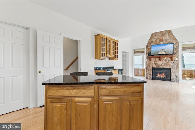 40461 Old Breton Beach Rd, Leonardtown, MD 20650 - kitchen featuring light wood-style flooring, dark stone counters, a stone fireplace, glass insert cabinets, and a kitchen island