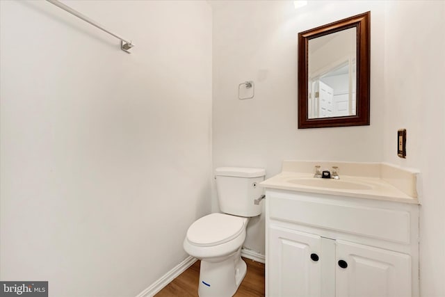half bathroom with toilet, baseboards, wood finished floors, and vanity