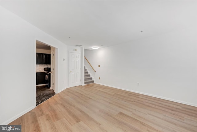 unfurnished room featuring light wood-type flooring, stairs, and baseboards