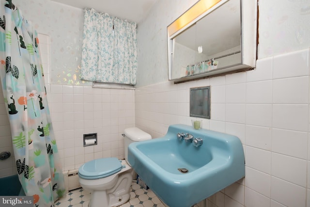 bathroom with wainscoting, toilet, tile walls, baseboard heating, and a sink