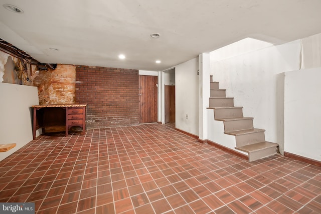 finished below grade area featuring stairs, recessed lighting, baseboards, and brick wall