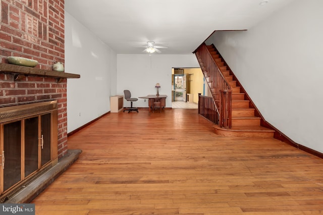 living room with a ceiling fan, a fireplace, baseboards, wood-type flooring, and stairs