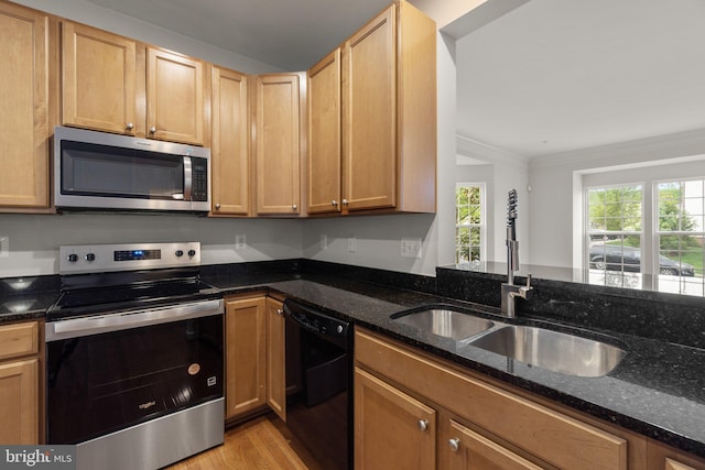 kitchen with appliances with stainless steel finishes, a sink, light wood-style floors, dark stone countertops, and crown molding