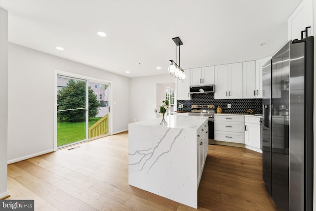 kitchen featuring a kitchen island, appliances with stainless steel finishes, light wood-type flooring, light stone counters, and white cabinetry