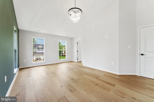 unfurnished living room featuring baseboards, light wood finished floors, a chandelier, and vaulted ceiling