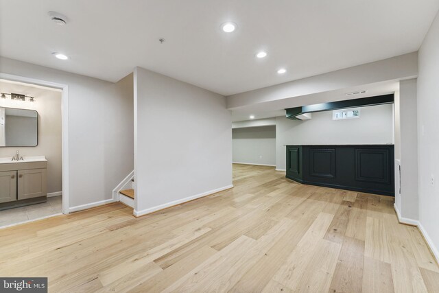 finished below grade area with light wood-style floors, a sink, and recessed lighting