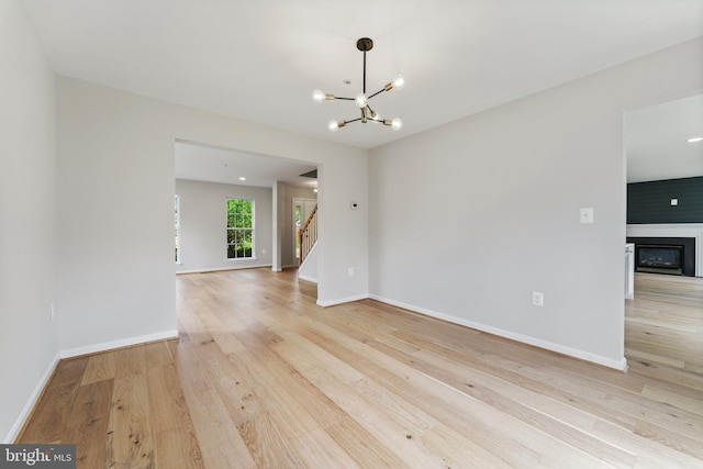 unfurnished room featuring stairway, baseboards, a glass covered fireplace, light wood finished floors, and an inviting chandelier