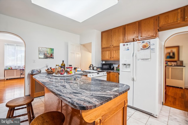 5506 39th Ave, Hyattsville, MD 20781 - kitchen featuring white appliances, brown cabinetry, light tile patterned floors, dark stone counters, and arched walkways