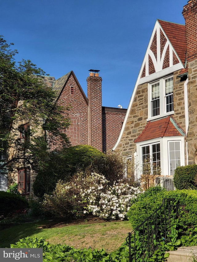 view of side of home featuring a high end roof, a chimney, and stone siding