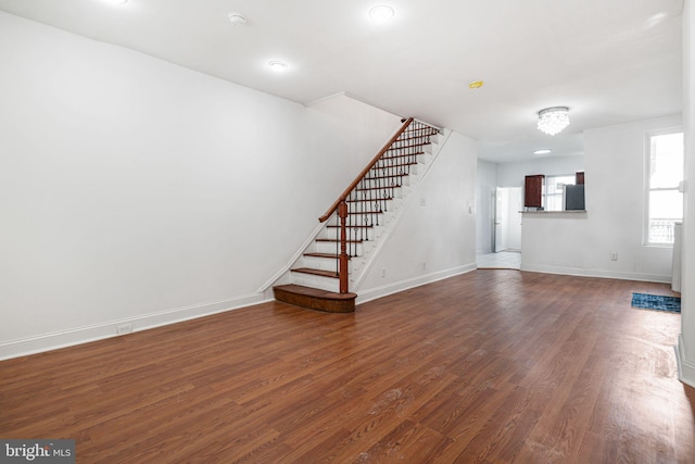 unfurnished living room with baseboards, dark wood-style flooring, and stairs