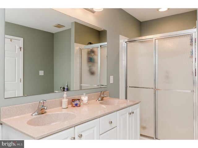 full bath with double vanity, visible vents, a shower stall, and a sink