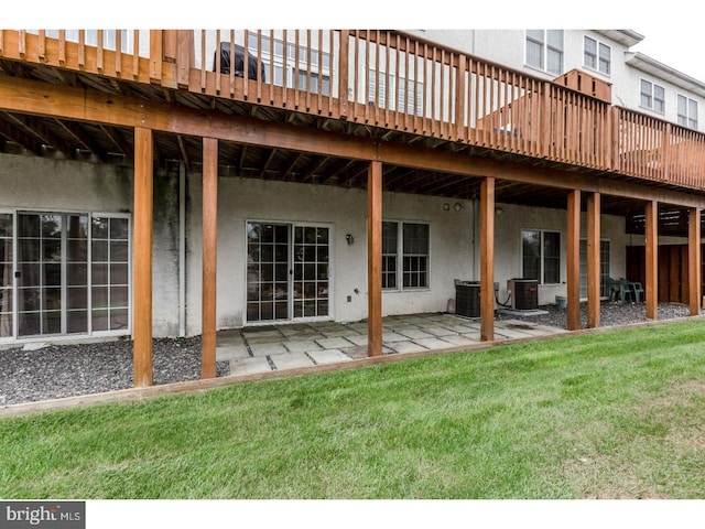 back of house featuring a lawn, a wooden deck, central air condition unit, a patio, and stucco siding