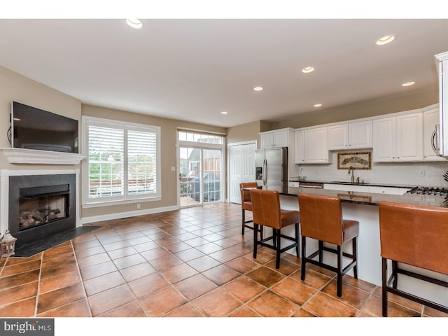 kitchen with open floor plan, a kitchen bar, stainless steel refrigerator with ice dispenser, white cabinetry, and a sink