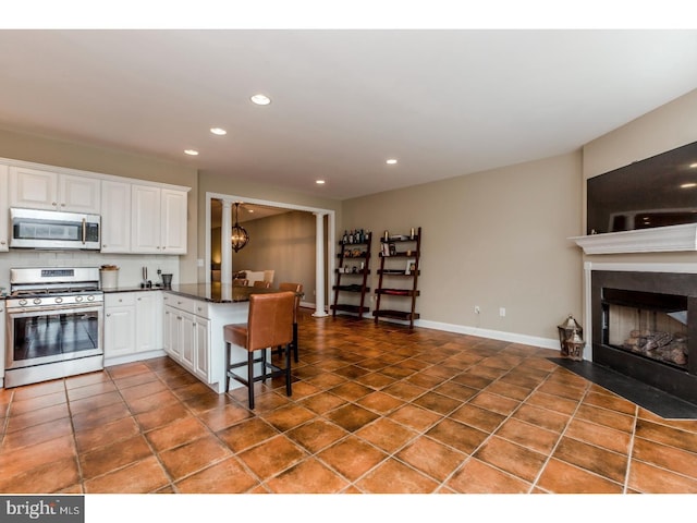 kitchen featuring dark countertops, stainless steel appliances, recessed lighting, white cabinetry, and a peninsula