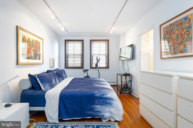 bedroom featuring a baseboard heating unit, rail lighting, and wood finished floors