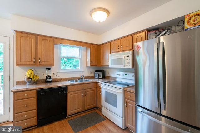 kitchen featuring light wood finished floors, brown cabinets, a sink, and white appliances