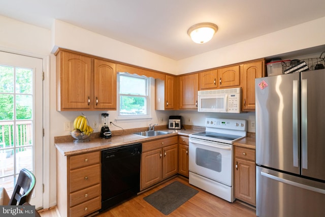 kitchen featuring a sink, brown cabinetry, white appliances, light wood finished floors, and light countertops