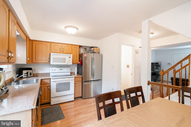 kitchen with a sink, white appliances, light countertops, and light wood-type flooring