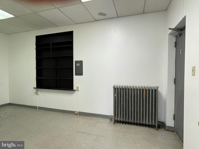spare room with baseboards, a drop ceiling, and radiator heating unit