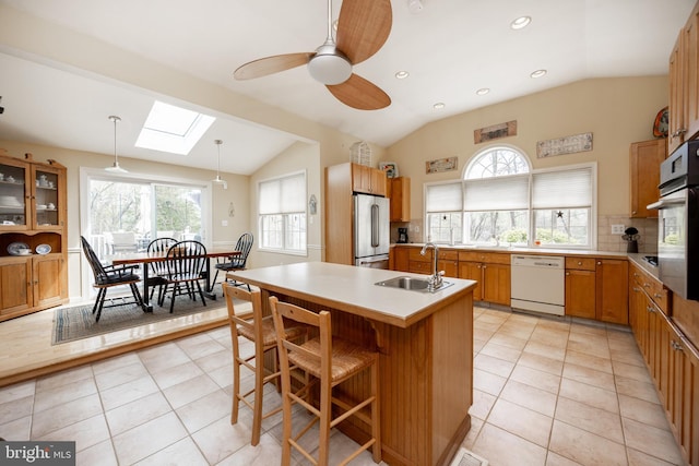 kitchen with a ceiling fan, appliances with stainless steel finishes, tasteful backsplash, a sink, and lofted ceiling with skylight