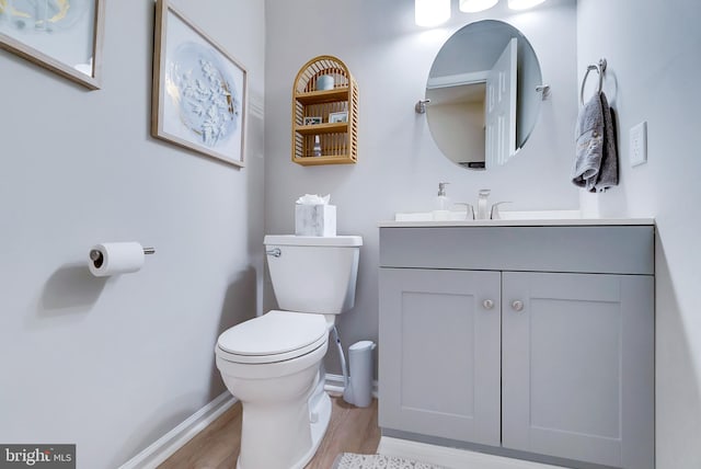 bathroom featuring toilet, baseboards, wood finished floors, and vanity