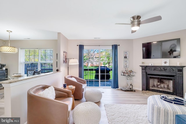 living room featuring a healthy amount of sunlight, ceiling fan, a fireplace, and wood finished floors