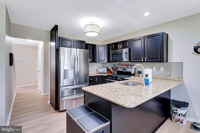 kitchen featuring a kitchen bar, appliances with stainless steel finishes, a sink, light stone counters, and a peninsula