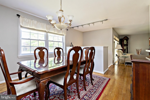 dining area with baseboards, an inviting chandelier, track lighting, and light wood finished floors