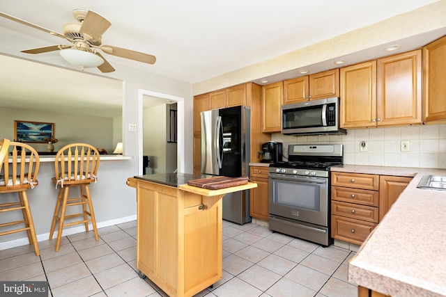 kitchen featuring a breakfast bar area, tasteful backsplash, light countertops, light tile patterned floors, and stainless steel appliances