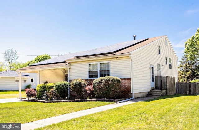 exterior space with roof mounted solar panels, fence, a lawn, and brick siding