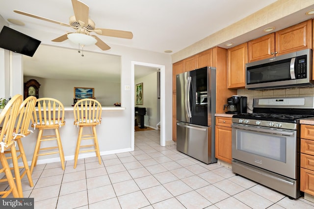 kitchen with ceiling fan, light countertops, stainless steel appliances, baseboards, and tasteful backsplash