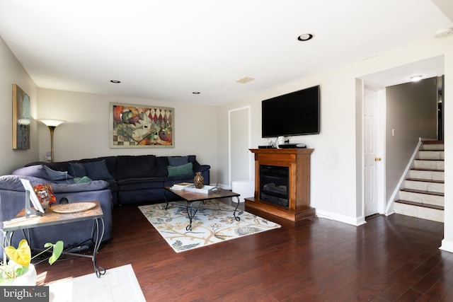 living room with baseboards, a fireplace with raised hearth, wood finished floors, and stairway