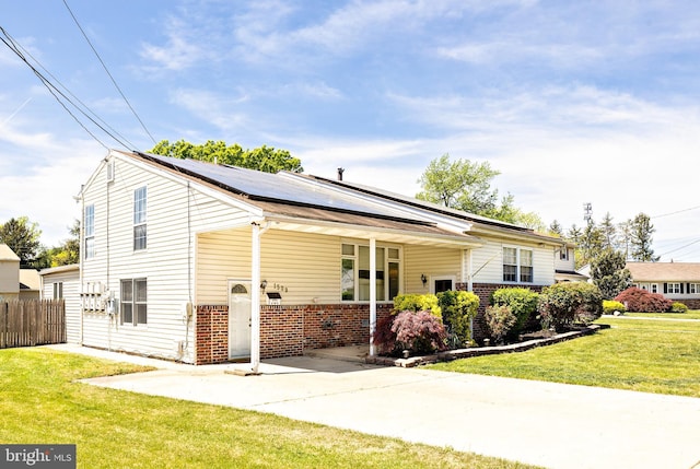 view of front of house featuring driveway, brick siding, fence, roof mounted solar panels, and a front lawn